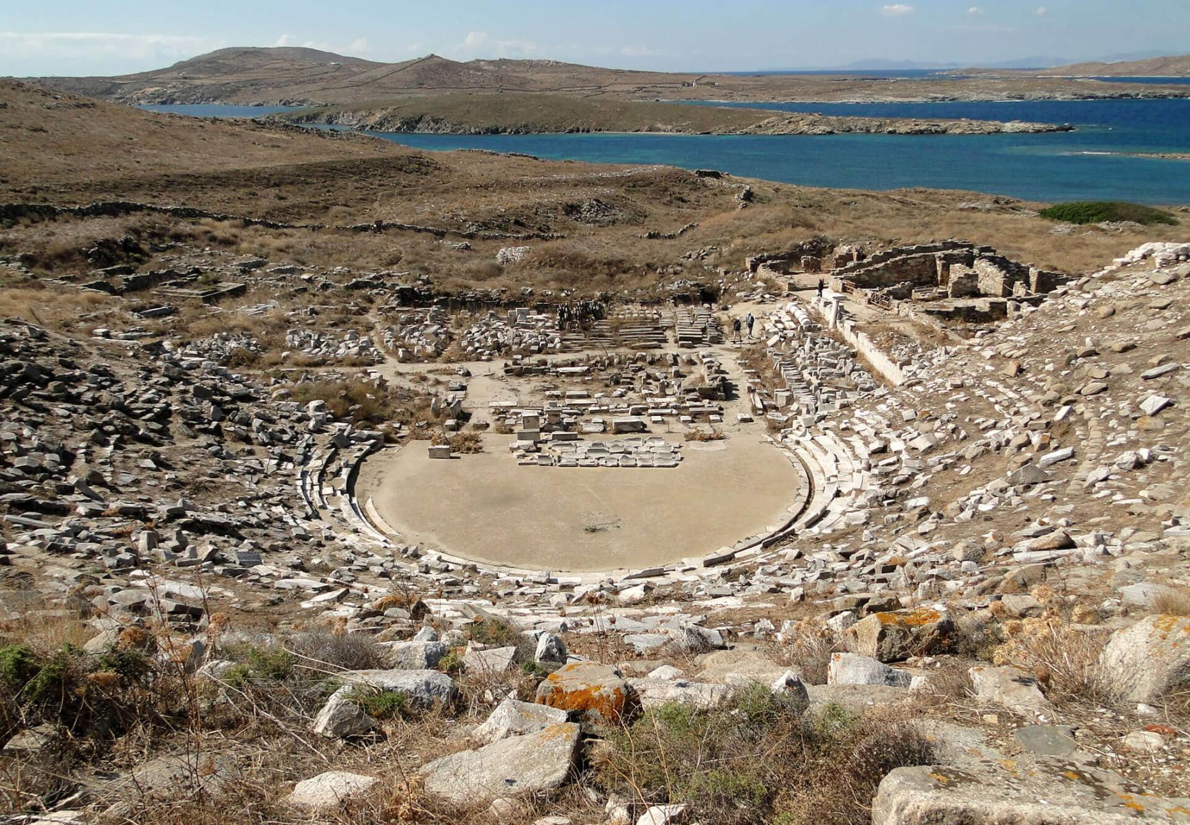View of the ancient theater at Delos, where performances took place, surrounded by historical ruins and columns.