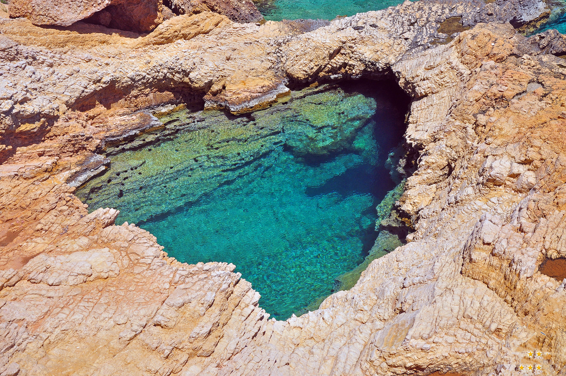Hidden natural pool in Koufonisia, formed by rock formations and filled with turquoise seawater.