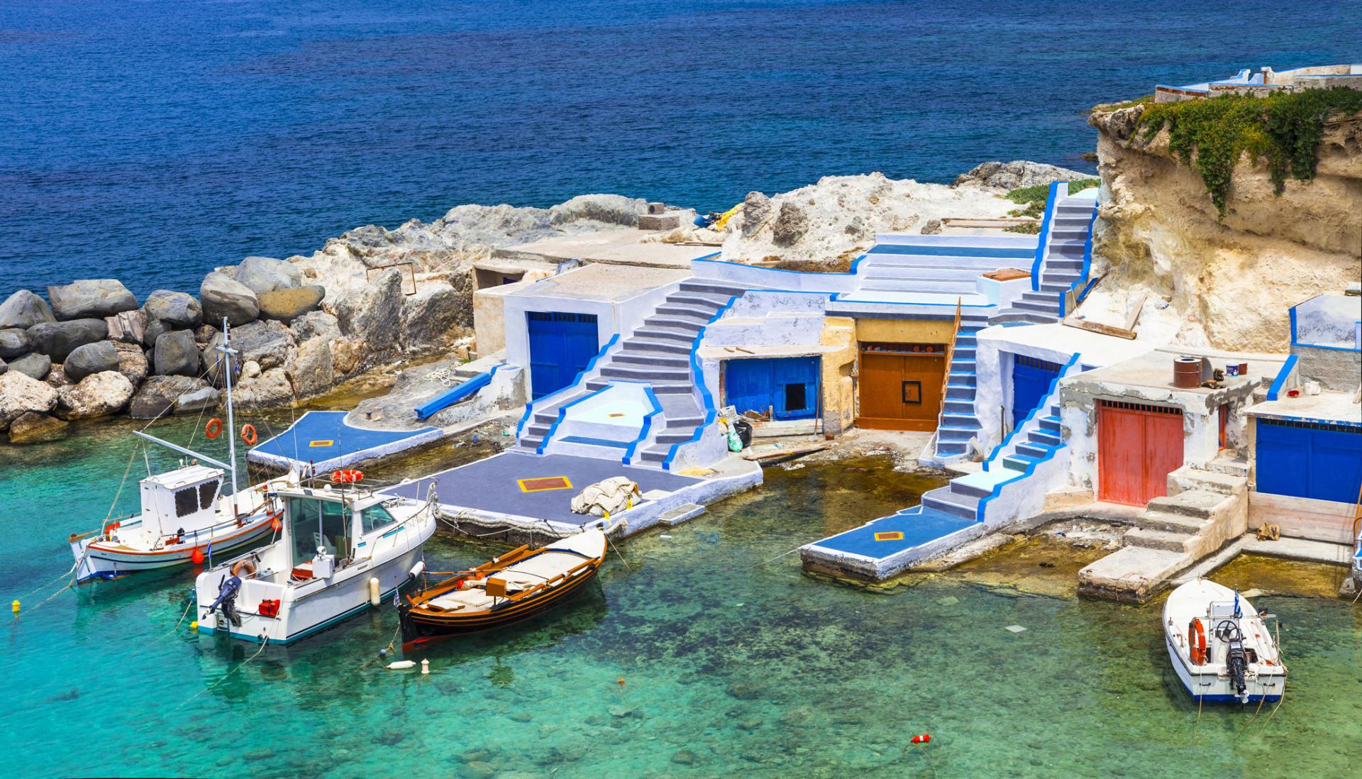 Traditional fishing village in Milos with colorful boats docked along the shore and charming whitewashed houses.