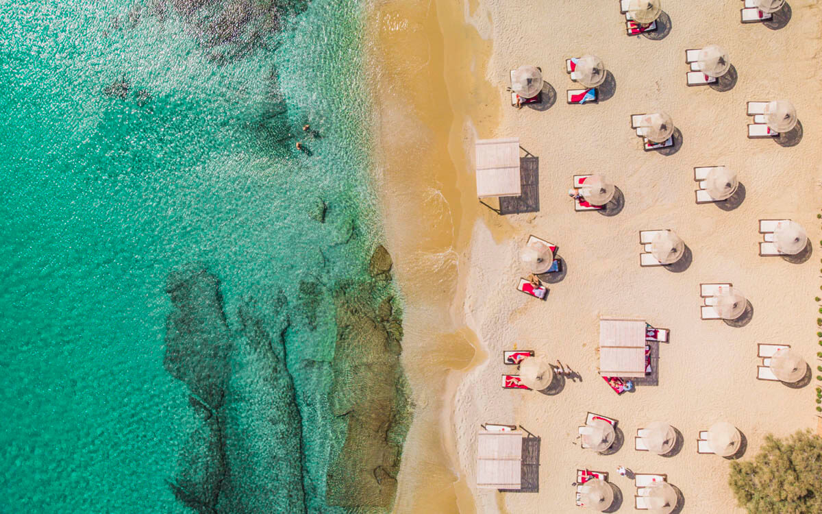 ibrant beach scene on Mykonos' south coast, with visitors relaxing under umbrellas and enjoying the Aegean sun