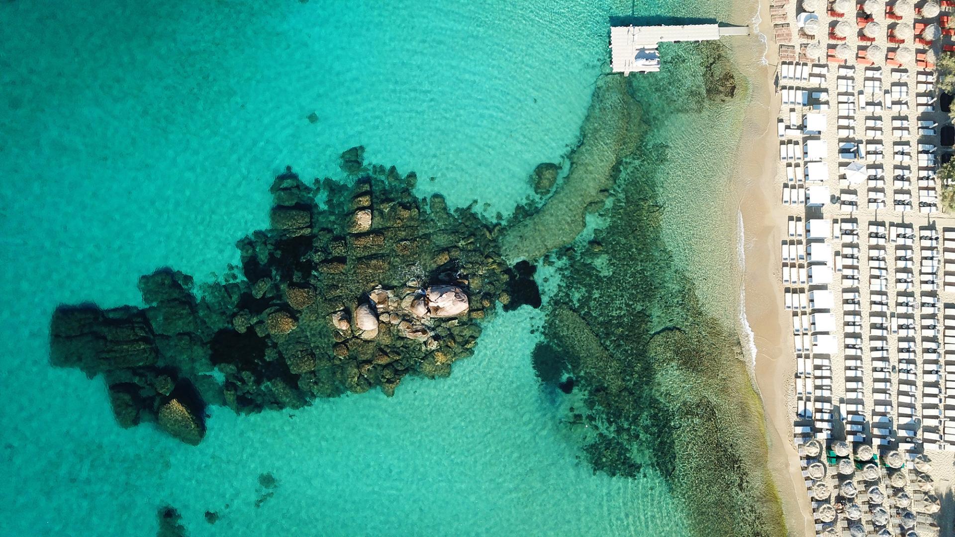 Golden sandy beach on the south coast of Mykonos, with crystal-clear turquoise waters and sunbeds lining the shore