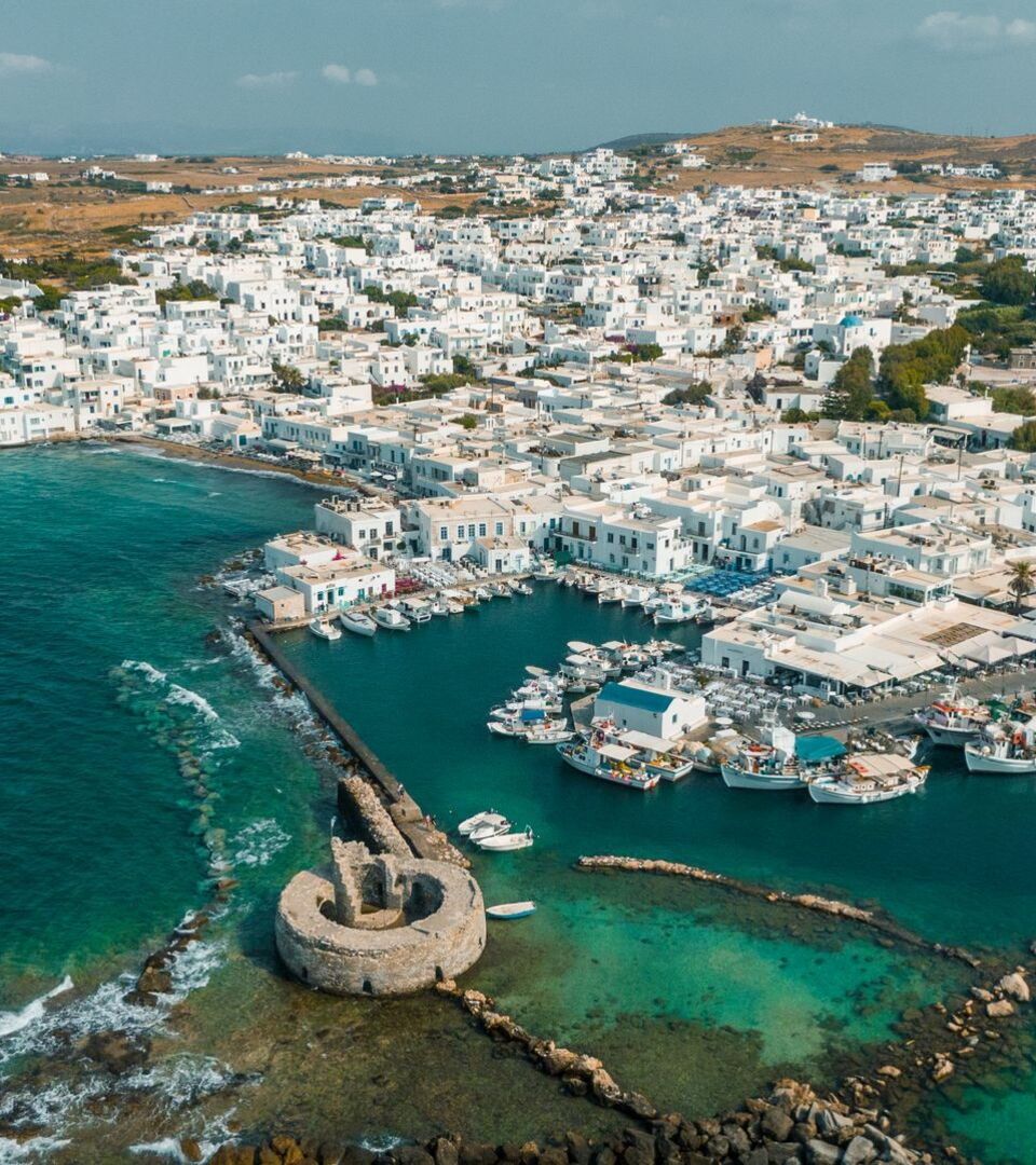 Aerial view of the port of Paros, showcasing ferries, sailboats, and the charming coastal town