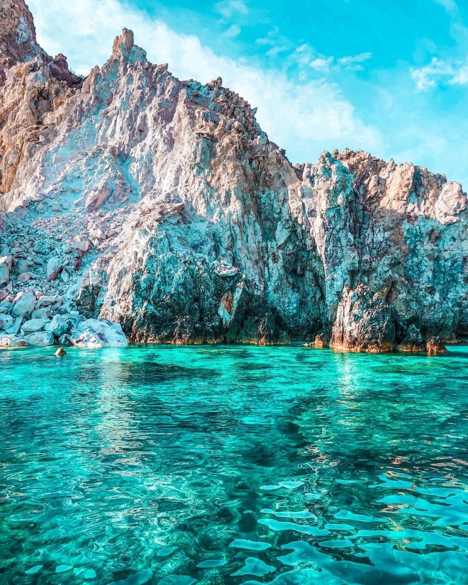 "Crystal-clear waters encircling the rocky landscape of Polyaigos Island, offering a serene and untouched setting.