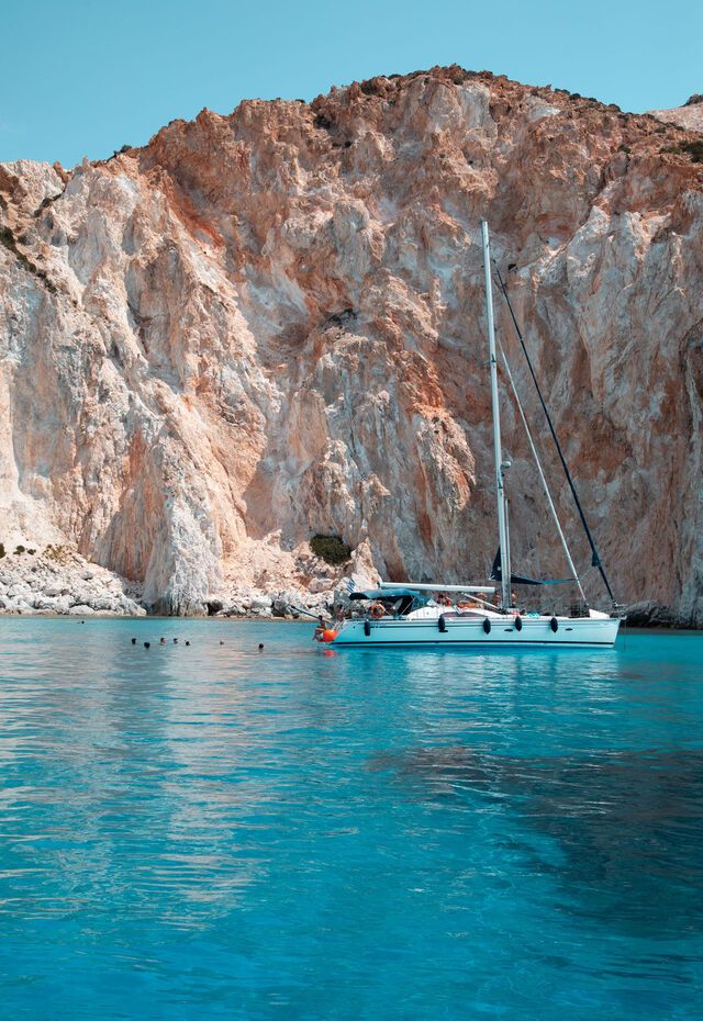 Polyaigos' pristine coast, with striking blue waters and rugged, sunlit rocks contrasting against the Aegean sky