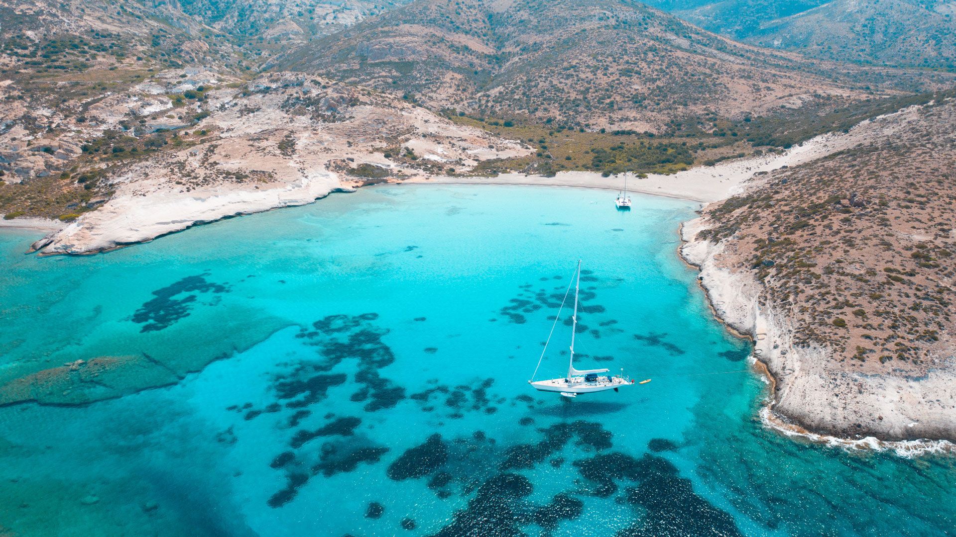 Pristine coastline of Polyaigos, with rocky cliffs surrounding a tranquil, hidden cove