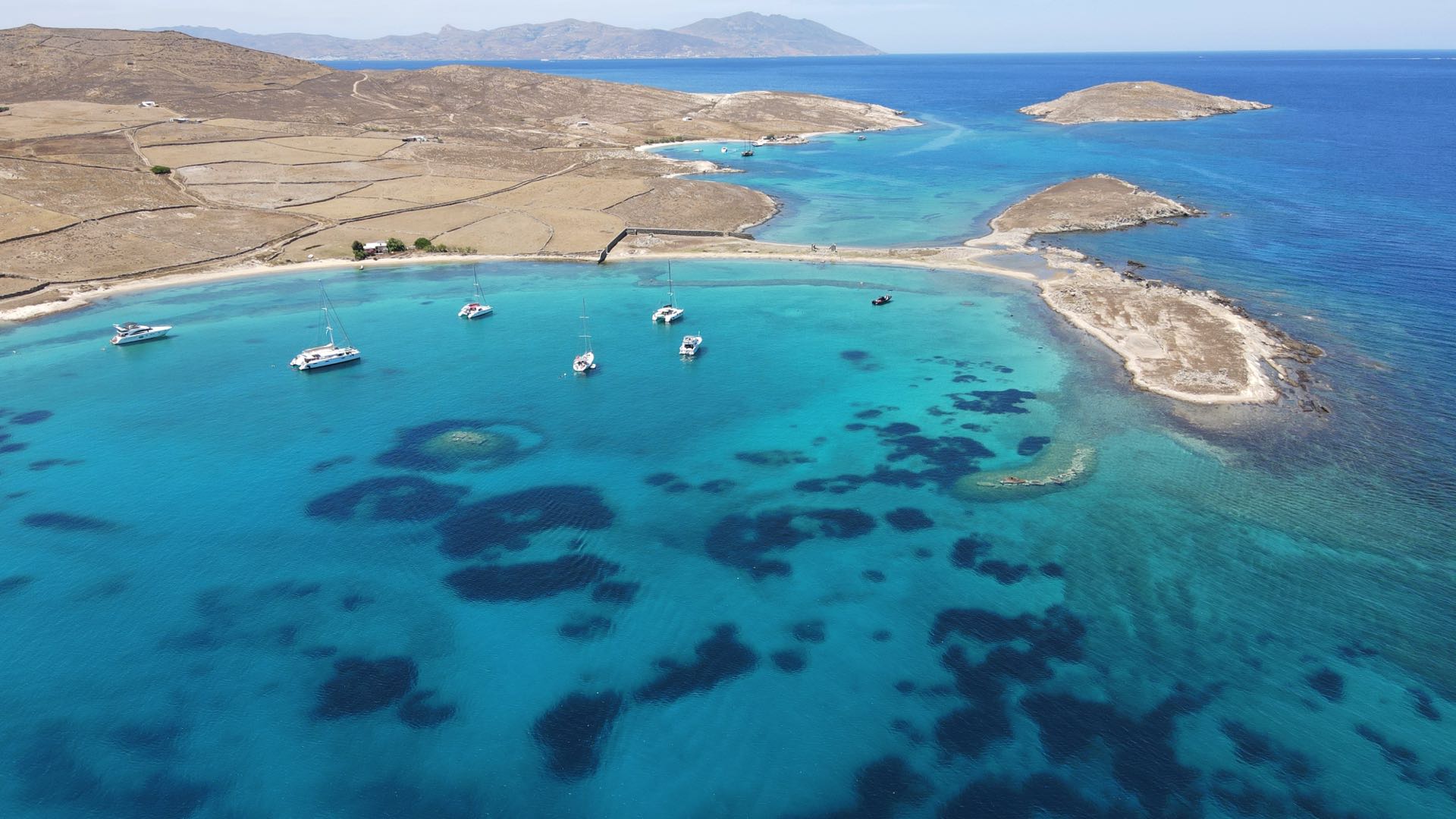 erial view of a hidden beach on Rhenia Island, with a yacht anchored nearby.