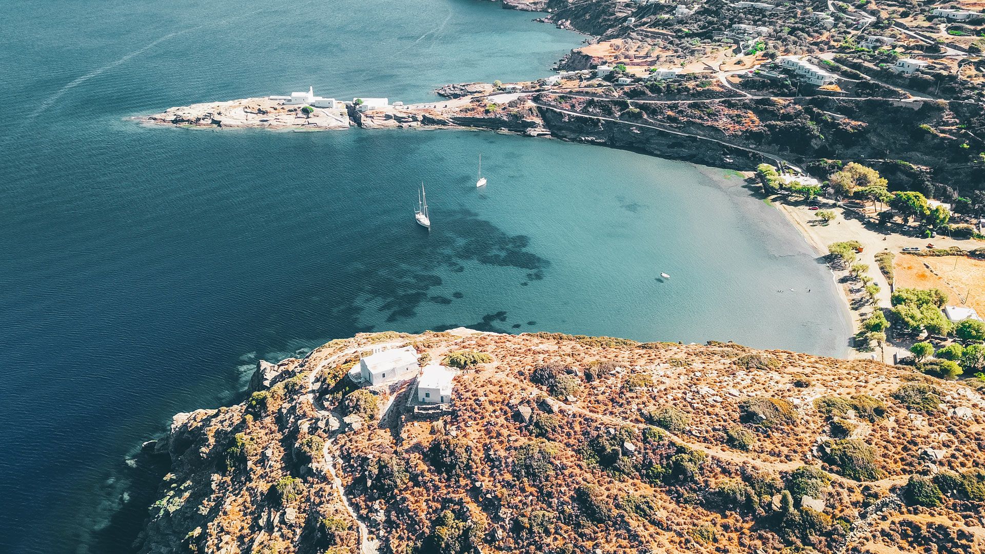 Aerial view of a breathtaking beach in Sifnos, with boats anchored in the blue waters.