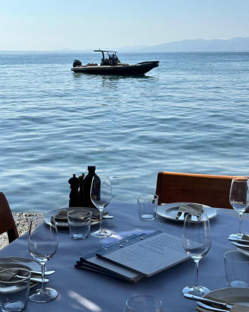 A cozy seaside restaurant in Tinos, where guests enjoy Greek cuisine with waves in the background.