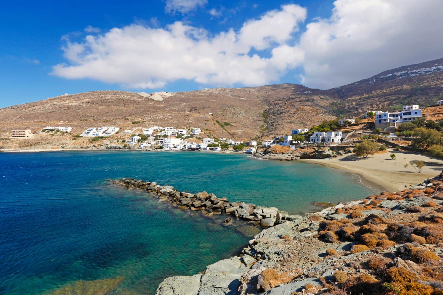 Golden sandy beach on Tinos Island with crystal-clear turquoise waters and rocky cliffs.