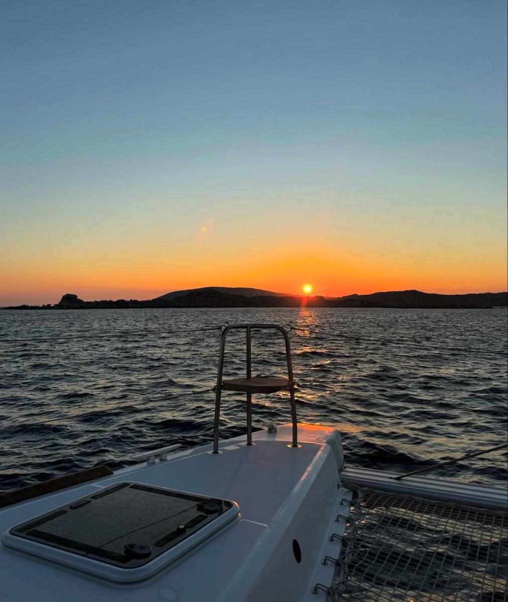 Guests watching a breathtaking sunset from the deck of a luxury yacht, with the Mykonos coastline in the distance