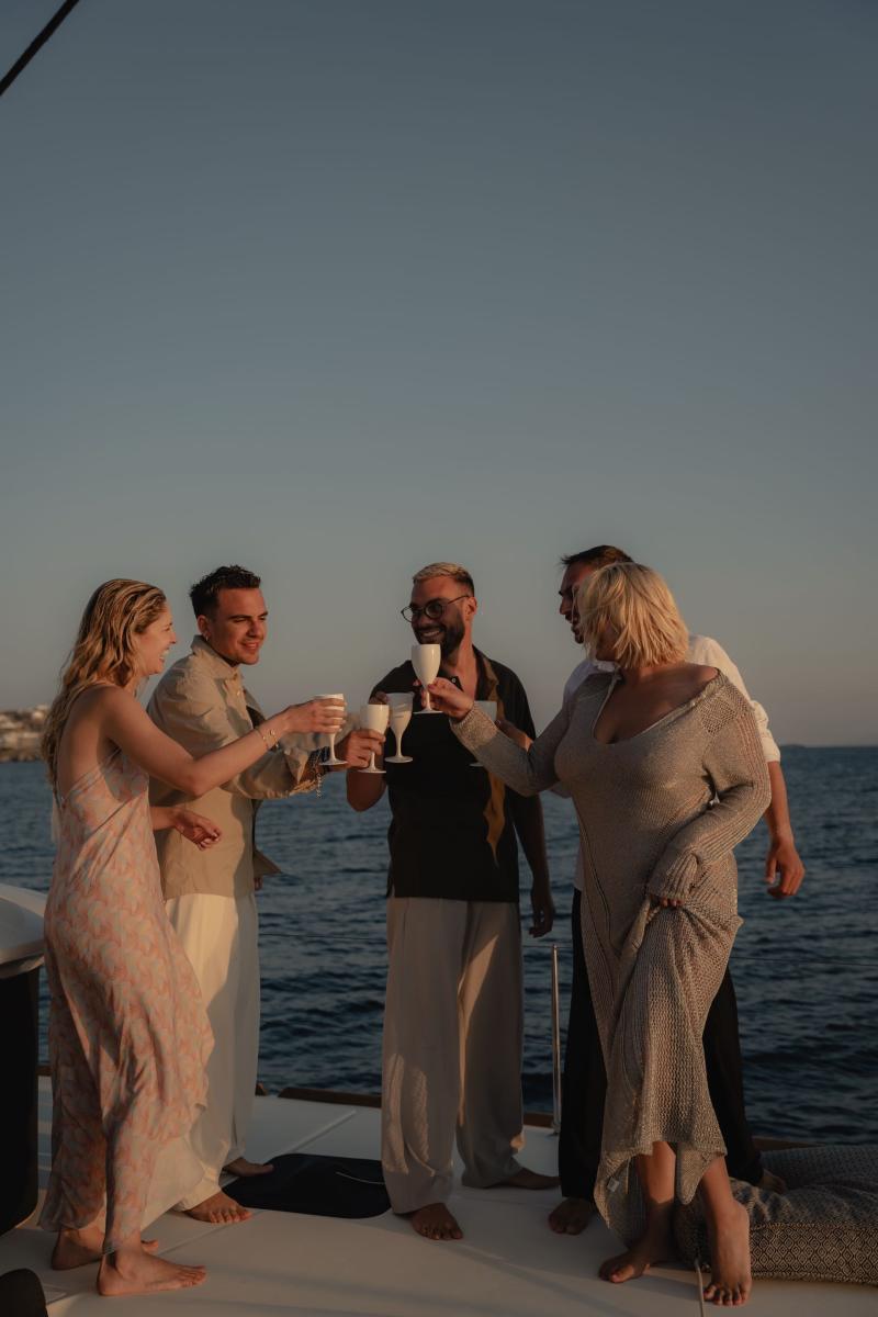 Guests toasting with champagne during a sunset cruise aboard a catamaran in Mykonos, with the golden sky reflecting on the water