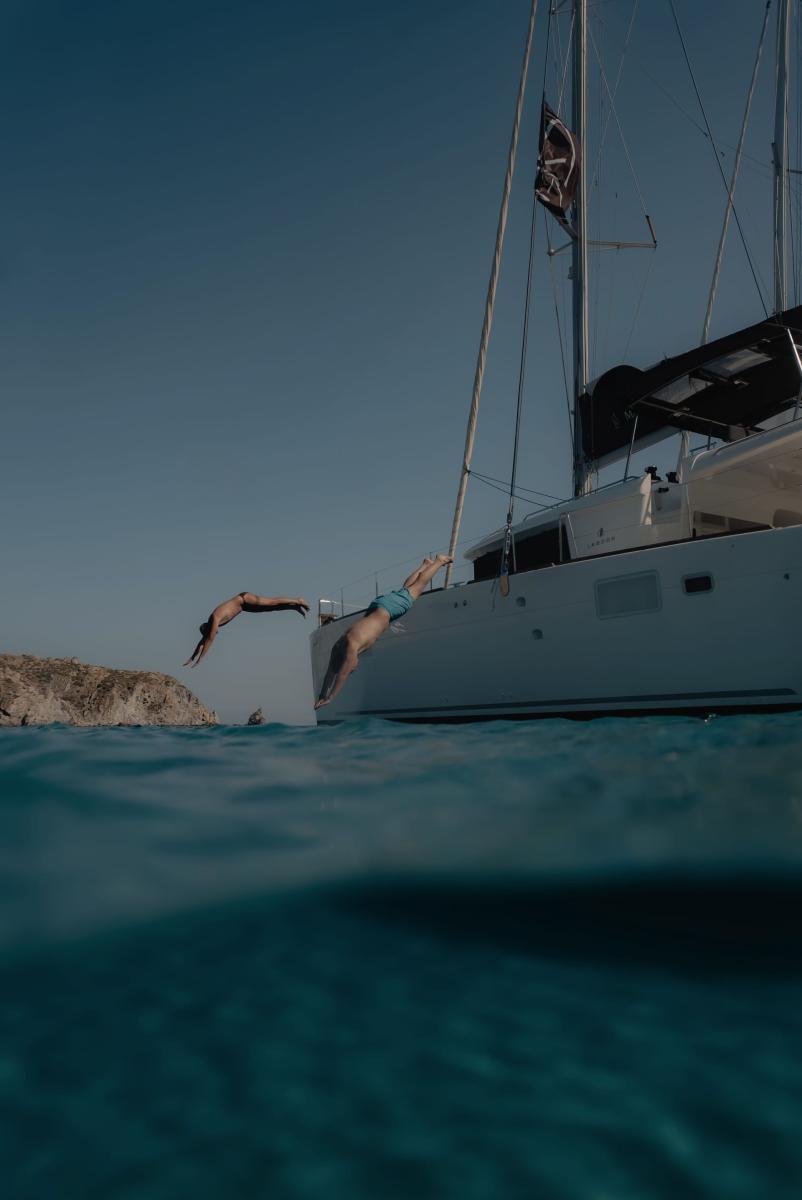 Adventurous guests diving off the side of a yacht into the refreshing waters of Mykonos, creating unforgettable memories
