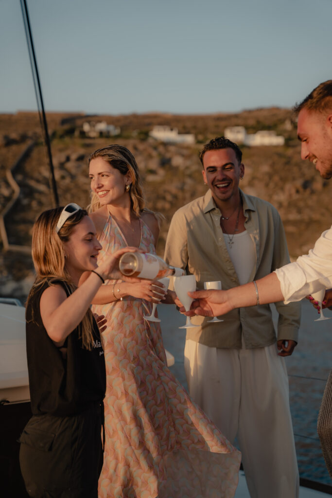 A group of friends cheers with cocktails on the deck of a catamaran, enjoying the lively vibes of Mykonos' crystal-clear waters