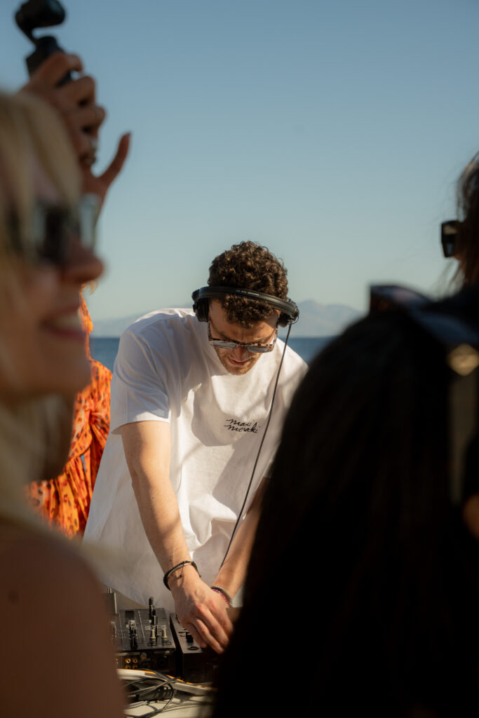 A DJ mixing music on the deck of a catamaran, creating a lively party atmosphere for guests in Mykonos