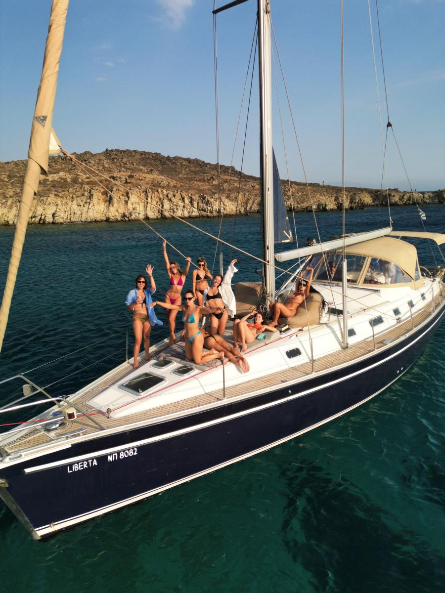 Guests Enjoying a Sailing Cruise in Mykonos – "A group of happy guests relaxing on the deck of a luxury sailing yacht, soaking in the stunning Aegean Sea views.