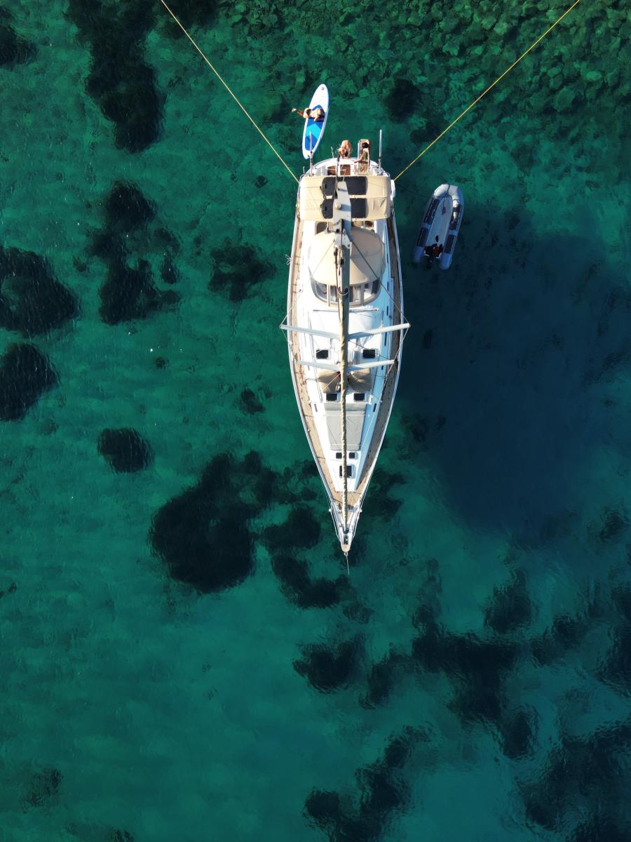 Sailing Yacht Anchored Near Rhenia Island – "A luxury sailing yacht anchored near Rhenia Island, surrounded by untouched natural beauty and pristine blue sea.
