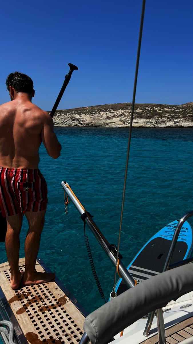 Paddleboarding from a Sailing Yacht – "A guest balancing on a paddleboard, exploring the calm waters around the yacht during a sailing cruise