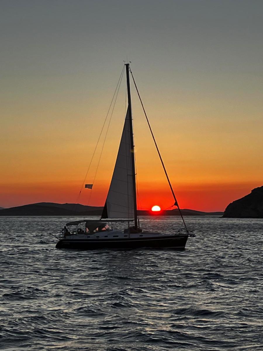 Breathtaking Sunset on a Mykonos Sailing Cruise – "Guests watching the sun dip below the horizon, painting the sky with golden hues during a sunset yacht cruise.