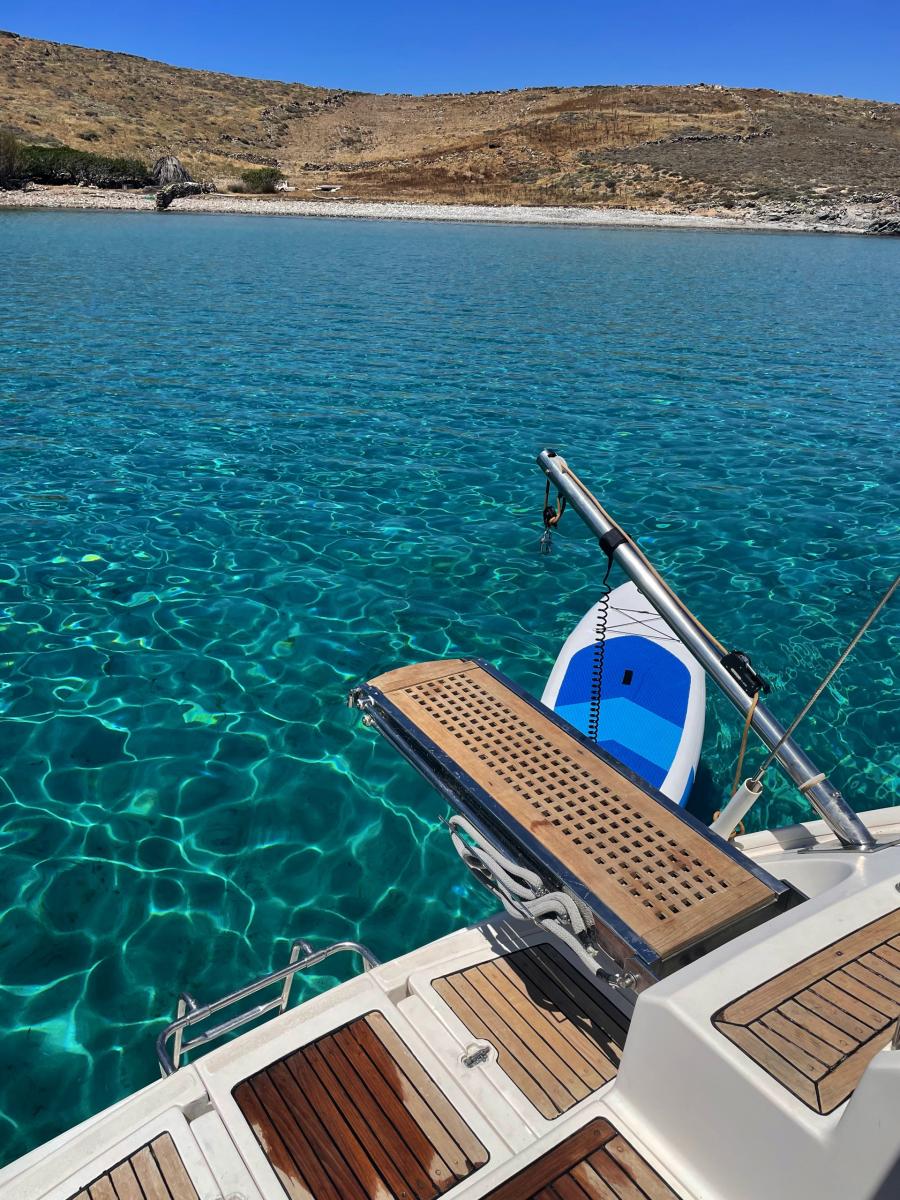 Paddleboarding from a Sailing Yacht – "A guest balancing on a paddleboard, exploring the calm waters around the yacht during a sailing cruise