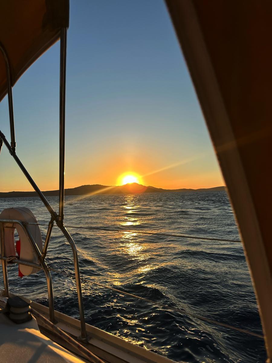 Breathtaking Sunset on a Mykonos Sailing Cruise – "Guests watching the sun dip below the horizon, painting the sky with golden hues during a sunset yacht cruise.